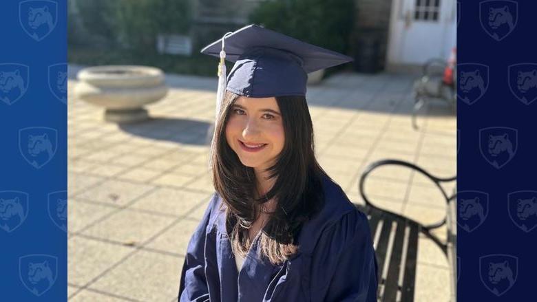 Student in cap and gown sitting outside